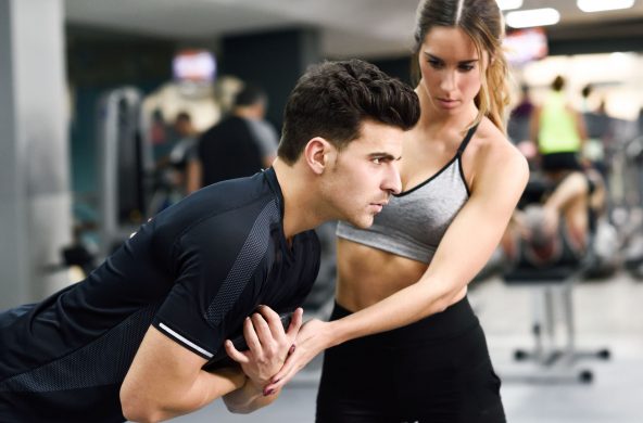 Female personal trainer helping a young man lift weights while working out in a gym